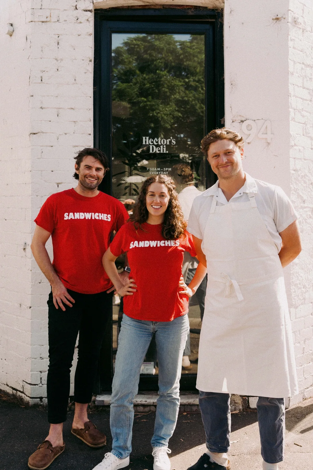 The Hector’s Deli team outside the shop, two in red Sandwiches t-shirts and the chef in a white apron