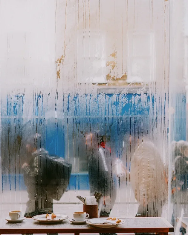 Coffee cups on a café table behind a fogged window, passers-by blurred outside