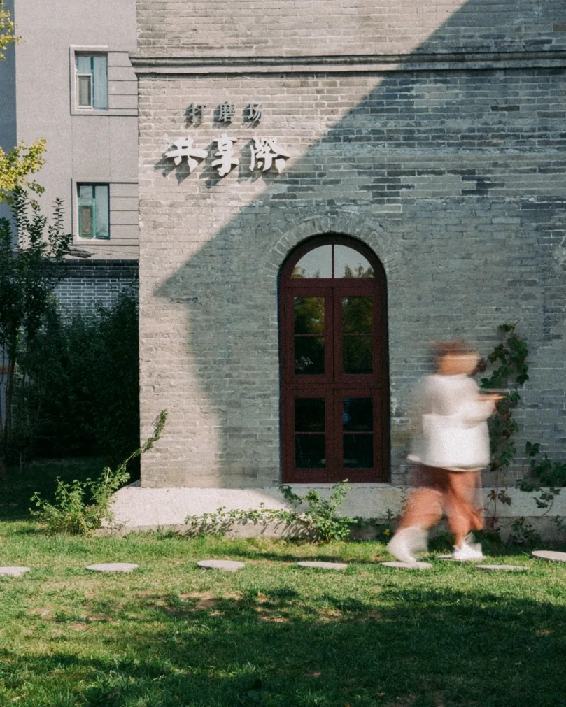 A figure in motion blur walking past a grey brick building with an arched red door