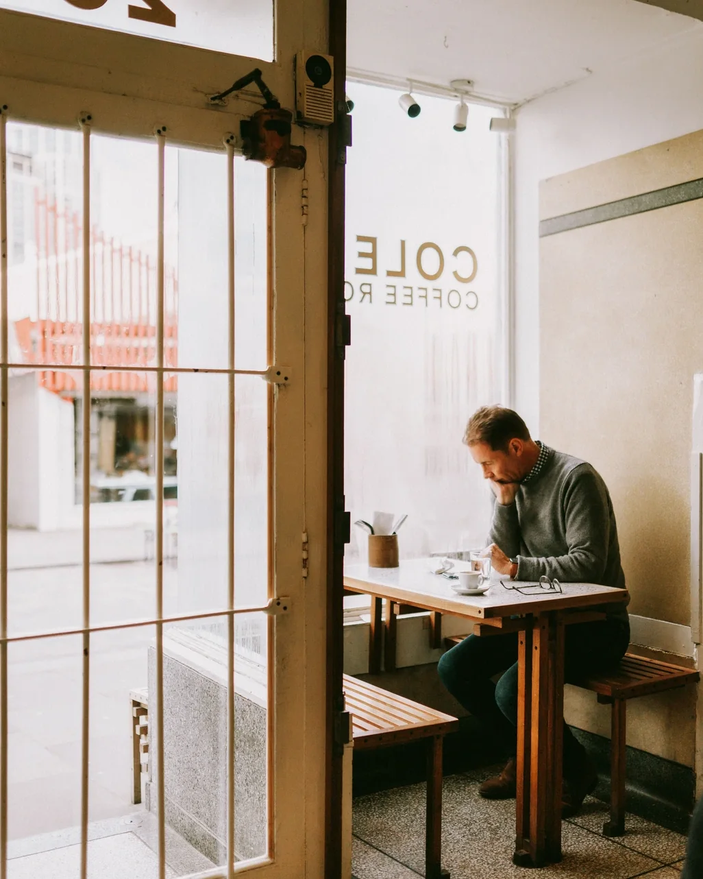 A man reading over coffee at a window table, seen through an open café door