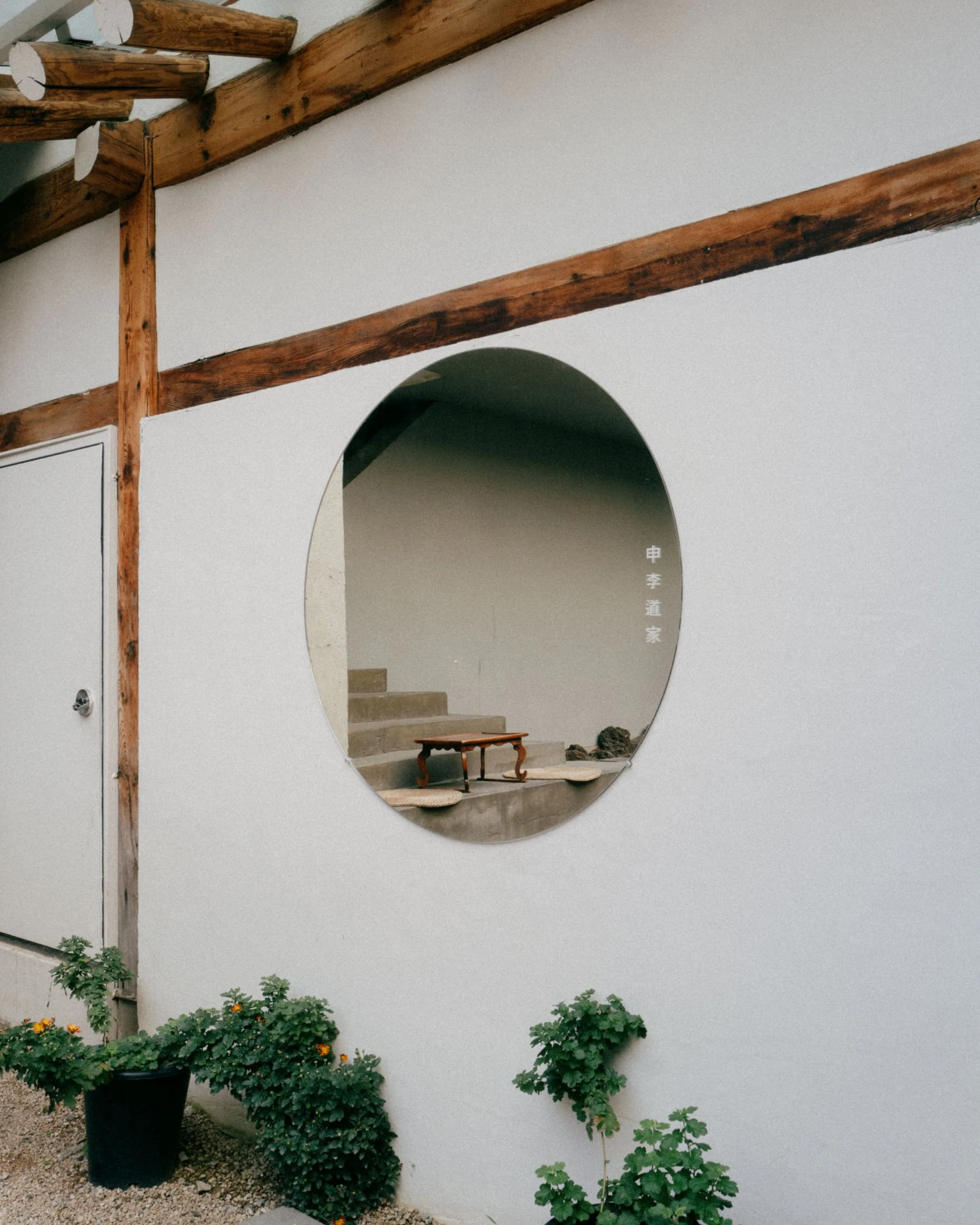 A round window in a white wall framing a low wooden table and woven cushions on concrete steps